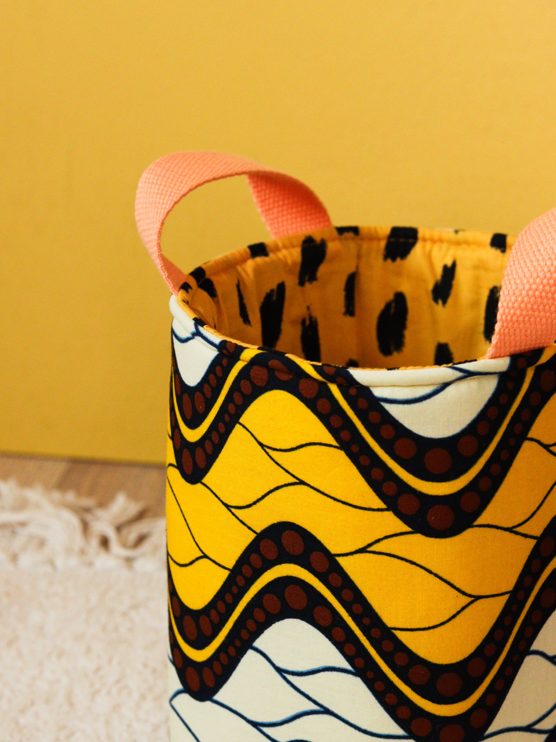 Détail anses panier déco S wax Savane posé sur un tapis, rangement coloré