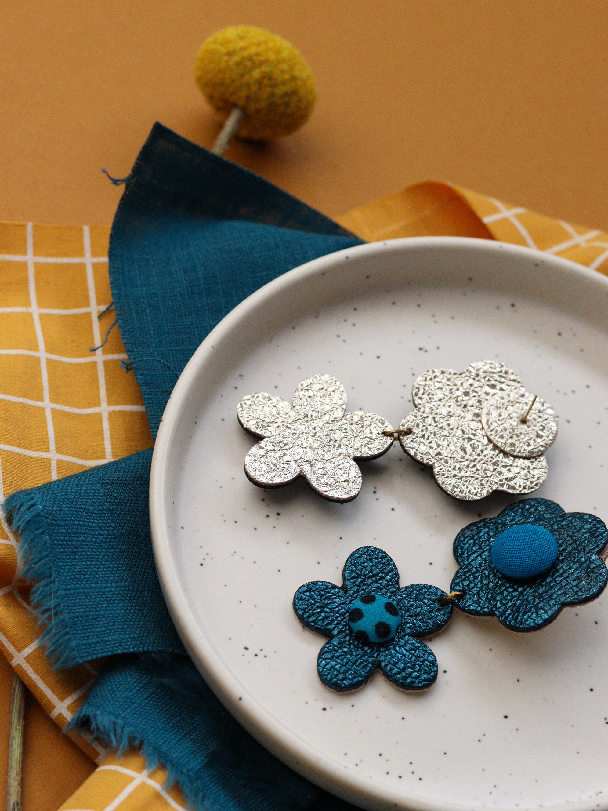 Détail de boucles d’oreilles deux fleurs en cuir bleu et tissu wax, fabrication artisanale, bretagne