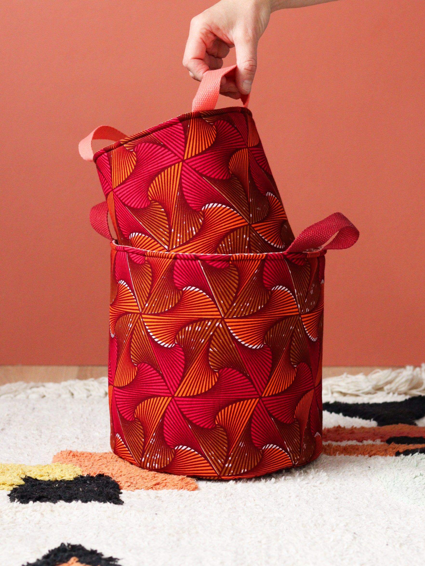 Paniers wax africain orange rose posés dans un salon coloré, mur terracotta